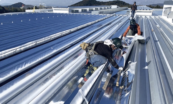 工場の屋根で遮熱シート施工をする作業員